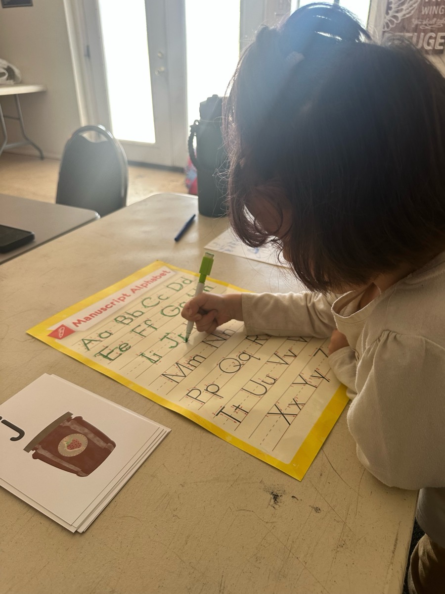 A young student tracing letters on a manuscript alphabet chart