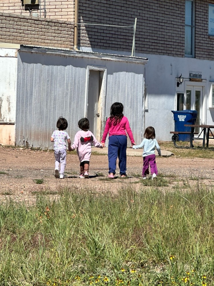 Four young students walking hand in hand across the school yard
